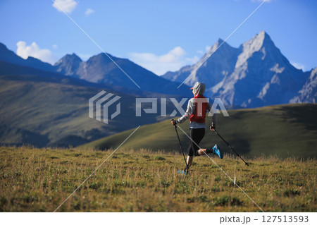 Fitness woman trail runner running in grassland with snow capped mountains in the background Fitness woman trail runner running in grassland with snow capped mountains in the background 127513593