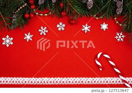 Christmas decorative set with green spruce, cones, holly berries, candy cane, white lace on red background, top view. Christmas decorative set with green spruce, cones, holly berries, candy cane, white lace on red background, top view. 127513647