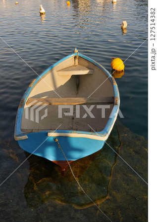 Old Dinghy Floating in Calm Harbor Waters at Sunset Old Dinghy Floating in Calm Harbor Waters at Sunset 127514382