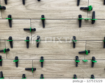 Tile installation in progress showing close up of wood look ceramic tiles with green and black leveling spacers. Ensuring precise alignment and even spacing during flooring renovation work 127515229