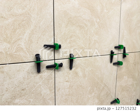 Beige marble style ceramic tiles installed with leveling system. Close up shows neat grout lines and surface alignment during precise wall finishing in interior remodeling 127515232