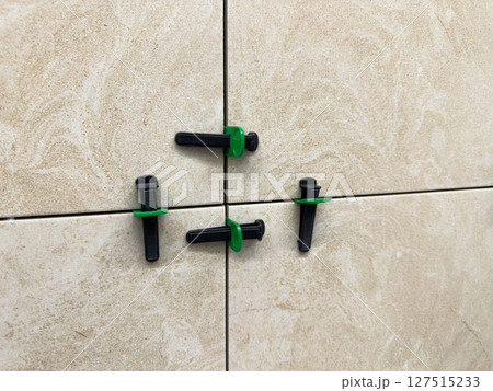 Ceramic wall tiles being installed with reusable leveling system. Black wedges and green spacers ensure even spacing and flat surface during home renovation and interior finishing 127515233