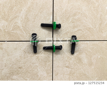 Close up of beige ceramic tiles aligned with tile leveling system. Precision tools create straight grout lines and a smooth, professional finish during modern interior installation work 127515234