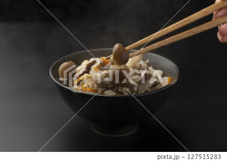 茶碗に盛り付けた土鍋で炊いたきのこの炊き込みご飯を箸で持ち上げる 127515283