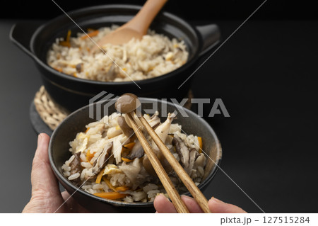 茶碗に盛り付けた土鍋で炊いたきのこの炊き込みご飯を箸で持ち上げる 127515284