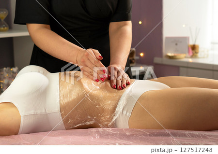 Therapist applies firm strokes over plastic-wrapped abdomen during session. 127517248