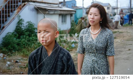 戦後の日本、廃墟の町を歩く和装の少年と母親 127519054