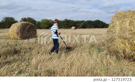 guy with a metal detector is looking for a treasure against the background of the field. teenage boy with a metal detector in his hands in search of treasure 127519723