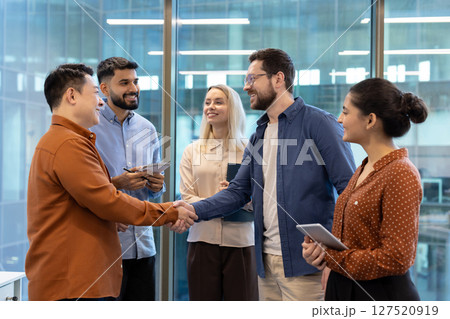 Diverse business team members shake hands in a modern office setting, symbolizing agreement and collaboration. 127520919