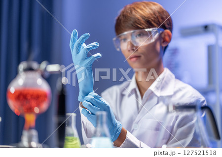 A young Asian male scientist putting on blue rubber gloves in the laboratory. A young Asian male scientist putting on blue rubber gloves in the laboratory. 127521518