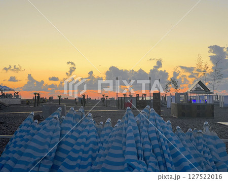 Colorful Blue and White Striped Umbrellas Stacked at a Sea Beach, Sunset Background 127522016