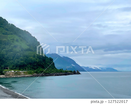 Calm Coastal View Featuring a Rocky Shoreline, Distant Mountains, and a Serene Sea Calm Coastal View Featuring a Rocky Shoreline, Distant Mountains, and a Serene Sea 127522017