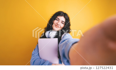 Smiling student taking selfie holding notebook and wearing headphones Smiling student taking selfie holding notebook and wearing headphones 127522431