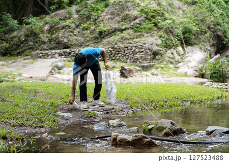 Volunteer Picking Up Waste. A young man collects plastic from a stream during a clean-up event. Volunteer Picking Up Waste. A young man collects plastic from a stream during a clean-up event. 127523488