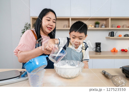 Family Cooking Fun. A mother pouring water while her son adds flour to a bowl. Family Cooking Fun. A mother pouring water while her son adds flour to a bowl. 127523550