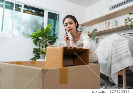 Moving process. Young woman packing boxes while on a phone call in a cozy home environment. 127523585