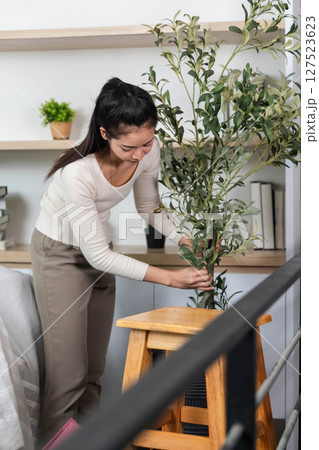 Setting up a new space. Woman arranging a plant in her home during the moving process. 127523623