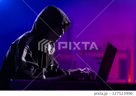 Young Man in Hoodie Working on Laptop in Dark Tech Environment Young Man in Hoodie Working on Laptop in Dark Tech Environment 127523990