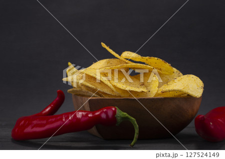 Chips with red pepper on a wooden plate on a gray background. 127524149