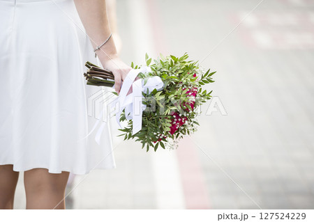 The bride's hand is casually holding a wedding bouquet. 127524229