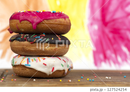Creative sweet food. A stack of glazed colorful assorted donuts on a bright watercolor painted background. 127524254