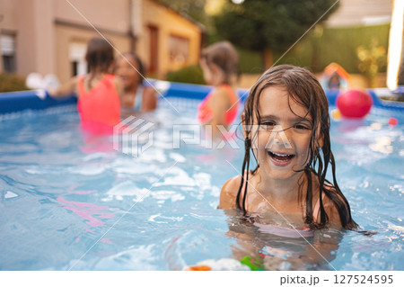 Young girl swimming joyfully in backyard pool during sunny day 127524595