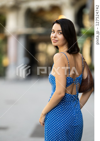 Young brunette girl in blue dress walking along the streets of the historical center of city 127524742