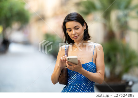 Happy young girl with mobile phone in her hands walking around city and taking pictures of sights Happy young girl with mobile phone in her hands walking around city and taking pictures of sights 127524898