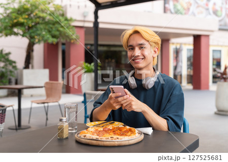 Thai gay teen male enjoying pepperoni pizza in outdoor restaurant 127525681
