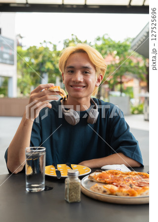 Thai gay teen male eating pepperoni pizza in outdoor restaurant 127525696