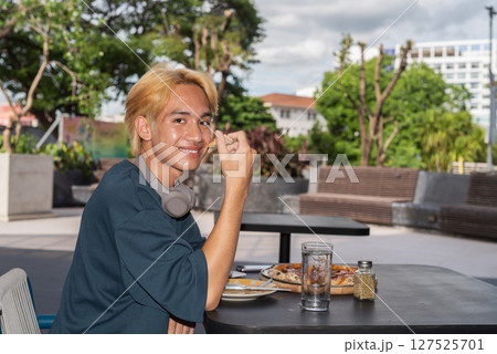 Thai gay teen male eating pepperoni pizza in outdoor restaurant 127525701
