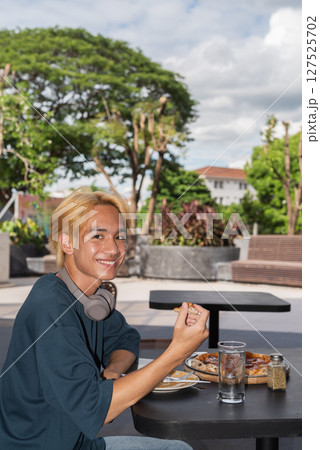 Thai gay teen male eating pepperoni pizza in outdoor restaurant Thai gay teen male eating pepperoni pizza in outdoor restaurant 127525702