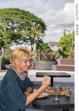 Thai gay teen male eating pepperoni pizza in outdoor restaurant Thai gay teen male eating pepperoni pizza in outdoor restaurant 127525703