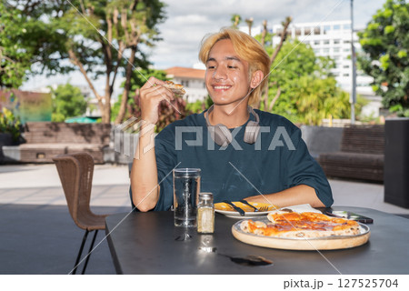 Thai gay teen male eating pepperoni pizza in outdoor restaurant Thai gay teen male eating pepperoni pizza in outdoor restaurant 127525704
