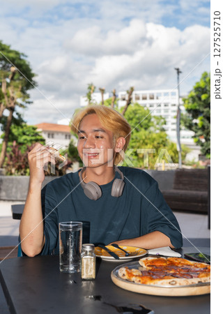 Thai gay teen male eating pepperoni pizza in outdoor restaurant Thai gay teen male eating pepperoni pizza in outdoor restaurant 127525710