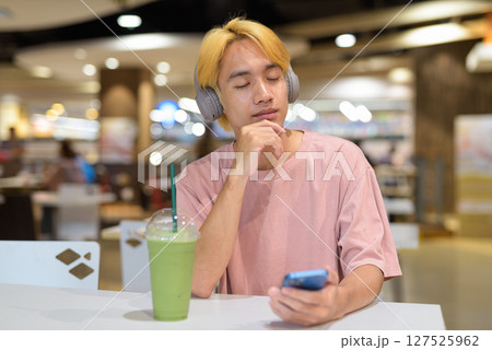 Thai gay teen man with headphones listening music in cafe Thai gay teen man with headphones listening music in cafe 127525962