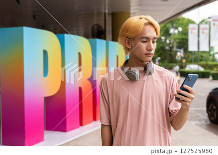 Young gay man using phone during pride festival Young gay man using phone during pride festival 127525980