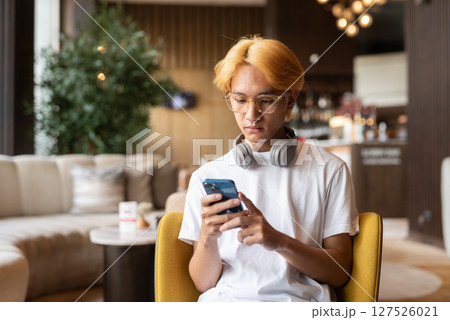 Asian teenager man with blonde hair inside cafe restaurant using phone 127526021