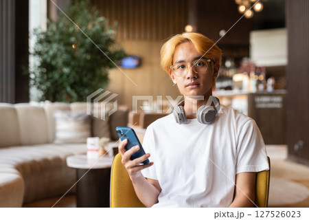 Asian teenager man with blonde hair inside cafe restaurant using phone 127526023