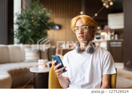 Asian teenager man with blonde hair inside cafe restaurant using phone 127526024