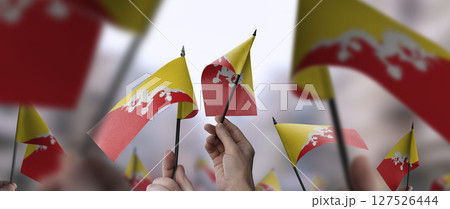 Bhutan flags in their hands on a blurred urban background Bhutan flags in their hands on a blurred urban background 127526444