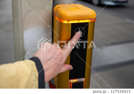 Pedestrian pressing button on traffic signal pole at crosswalk in city street Pedestrian pressing button on traffic signal pole at crosswalk in city street 127526815