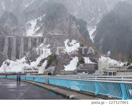 吹雪の中の観光名所立山黒部アルペンルートの立山連峰の雪景色と黒部ダムの様子 127527001