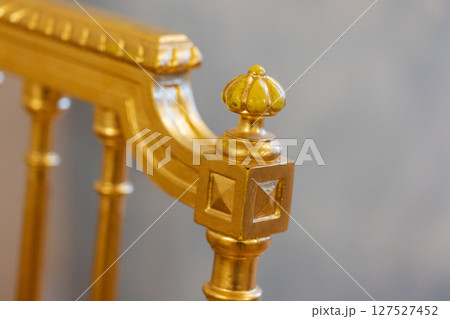 Detailed view of an ornate golden chair featuring an intricate crown finial design 127527452