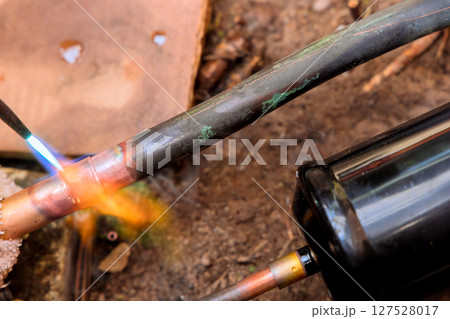 Copper tube is being soldered in garden setting using flame for plumbing repair work. 127528017