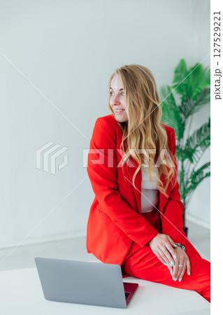 Business woman in red suit at desk with laptop working in office Business woman in red suit at desk with laptop working in office 127529221