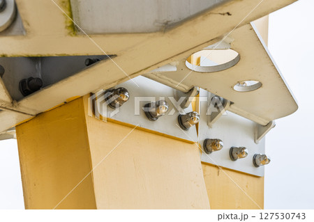 Bolted gusset plates securing yellow steel beam to column, structural engineering close up 127530743