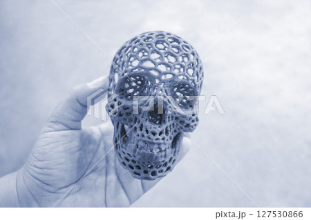 Art model of human skull printed on a 3D printer from molten plastic in hand. Object human skull created by 3D printer from molten plastic. Modern additive 3D printing technologies. FDM technology 127530866