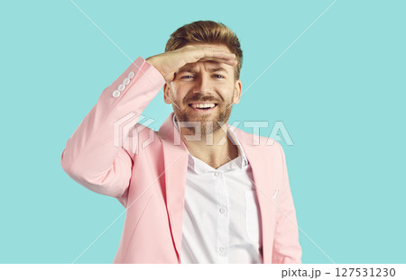 Happy young man in pink suit holds his hand on forehead above eyes and looks in distance 127531230