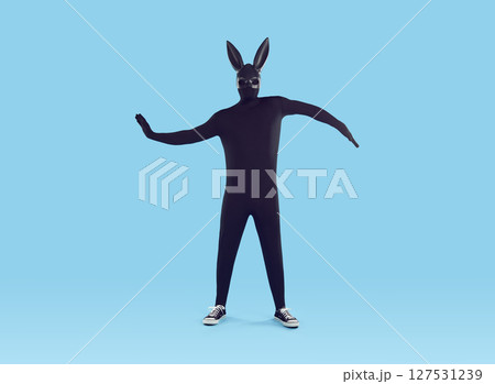 Faceless man wearing black bodysuit costume with hare mask having fun on blue background. 127531239